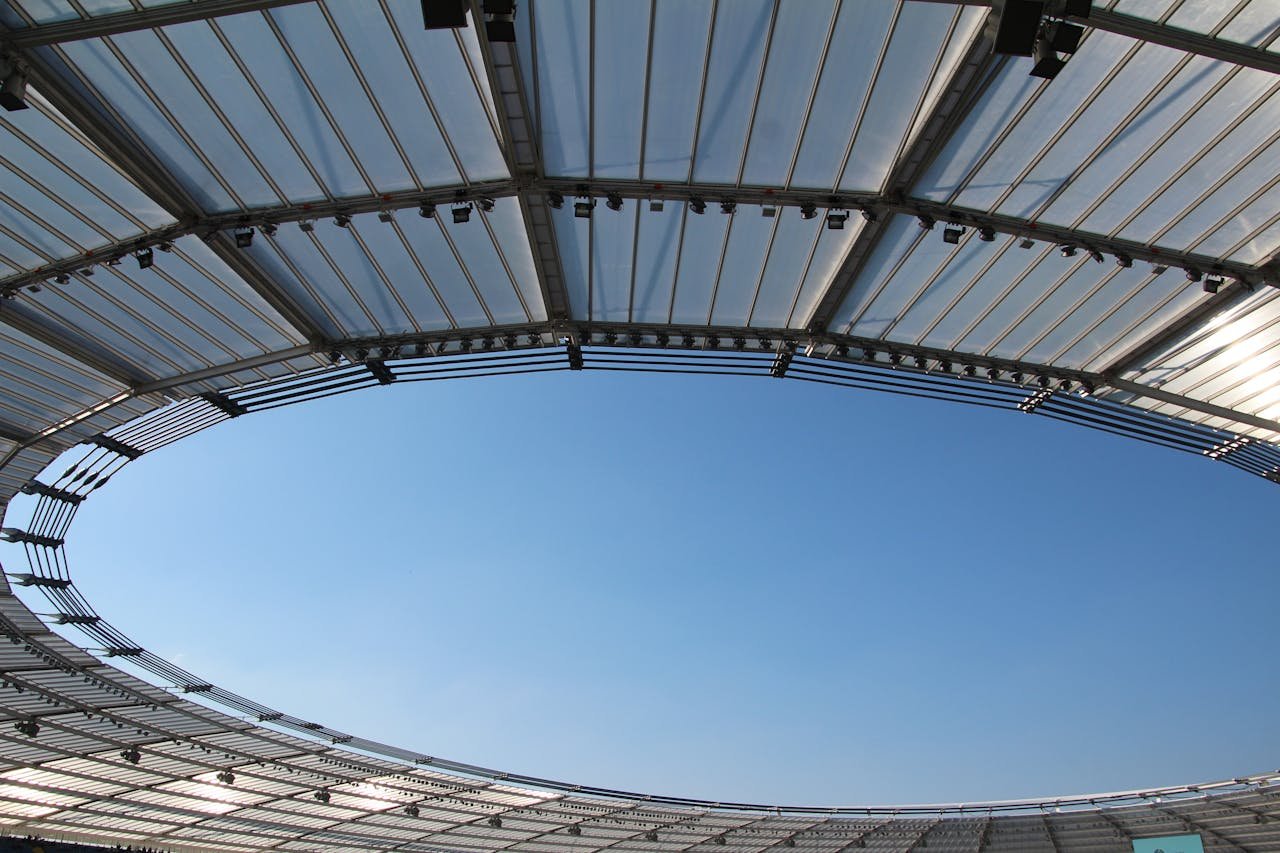The Art of Drawing Readers In: Your attractive post title goes here A modern stadium roof design framing a clear blue sky, illustrating structural elegance and openness.
